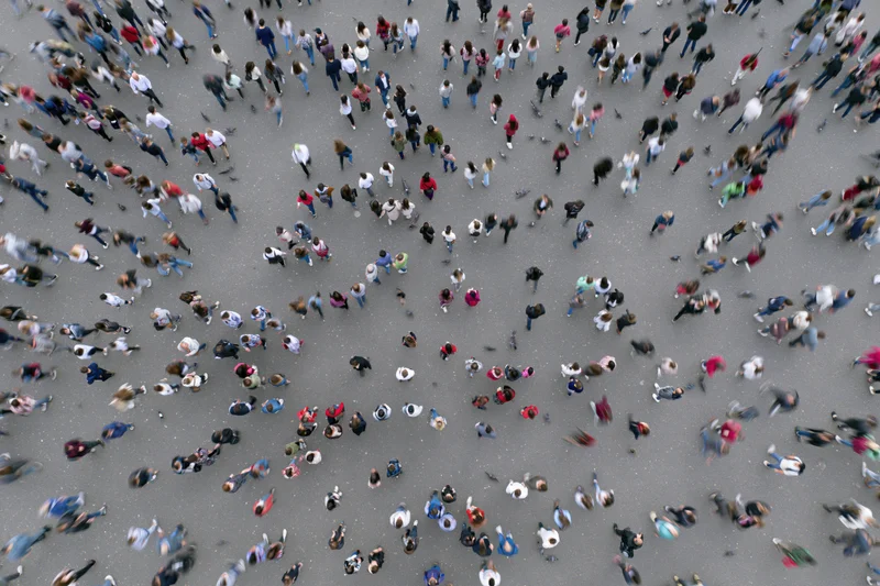 Aerial top-down view of a dense crowd of people walking across a city street