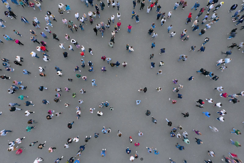 Aerial top-down view of a dense crowd of people walking across a city pavement