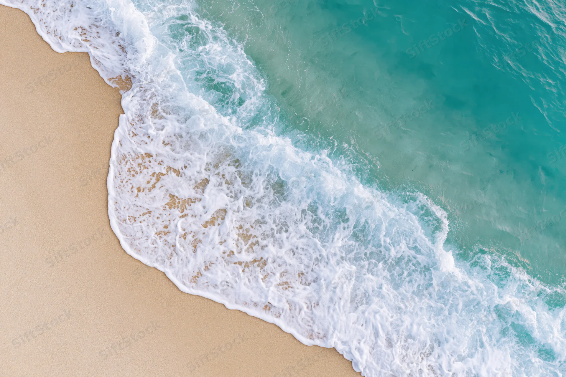 Aerial top-down view of a gentle ocean wave washing onto a sandy beach