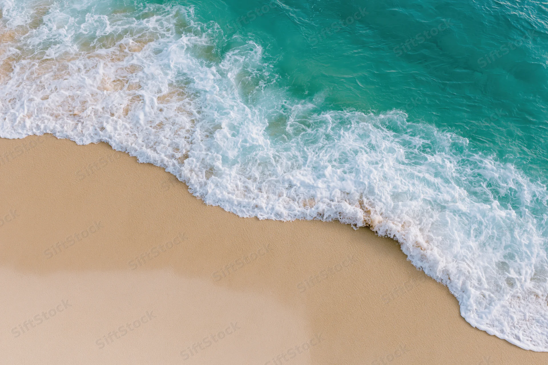 Aerial top-down view of a gentle ocean wave washing onto a sandy beach
