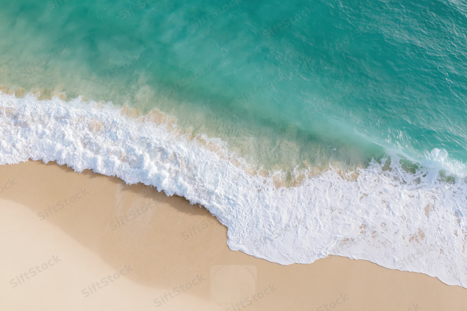 Aerial top-down view of a gentle ocean wave washing onto a sandy beach