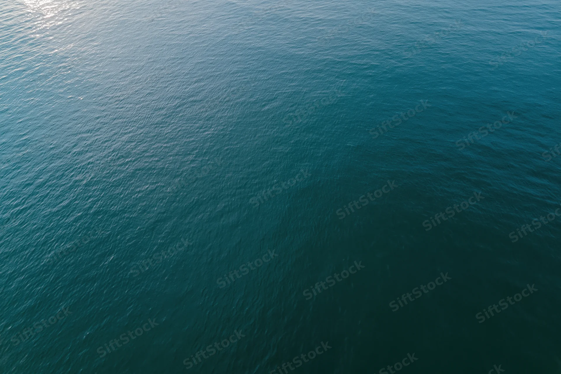 Aerial top-down view of calm open water surface with sunlight reflection