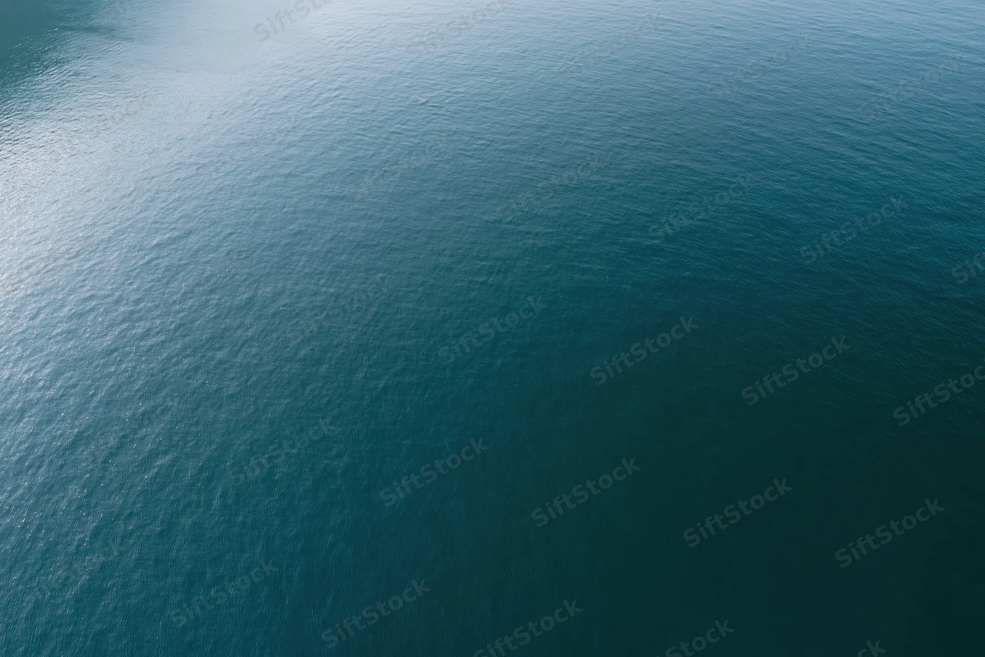 Aerial top-down view of calm open water surface with light reflections and subtle ripples