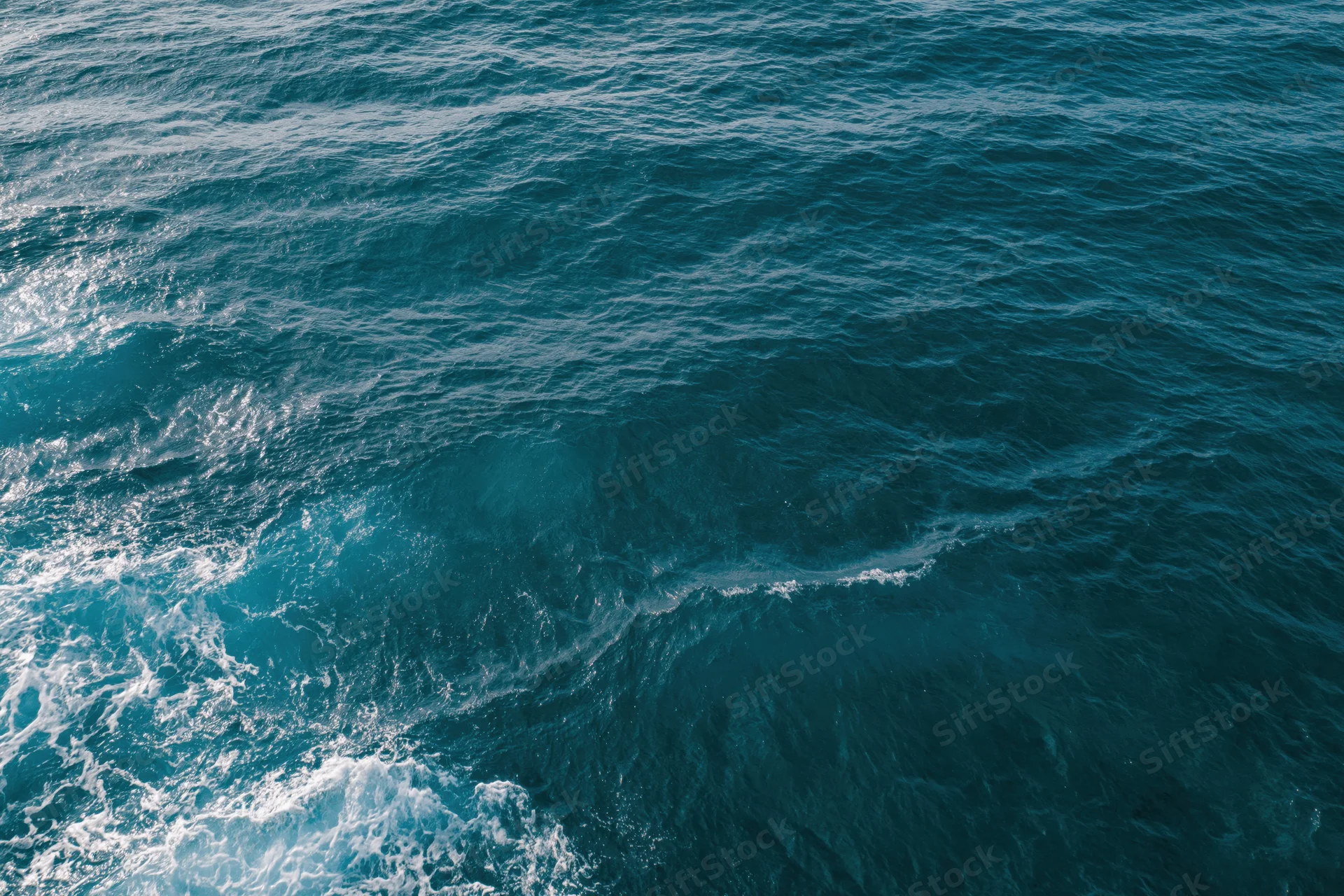Aerial top-down view of open ocean surface with small ripples and white foam