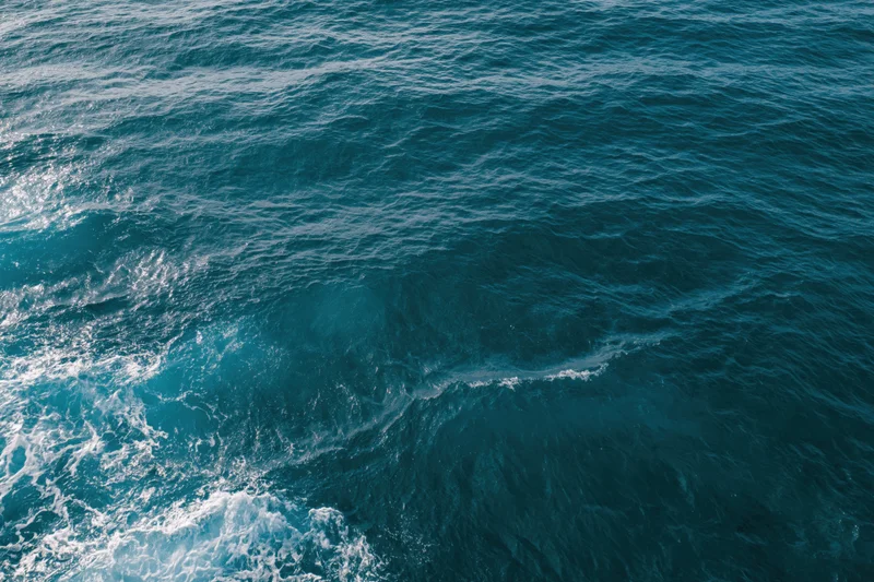 Aerial top-down view of open ocean surface with small ripples and white foam