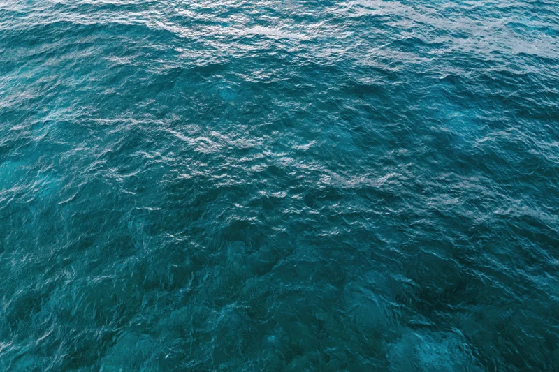 Aerial top-down view of open ocean surface with small ripples and light reflections