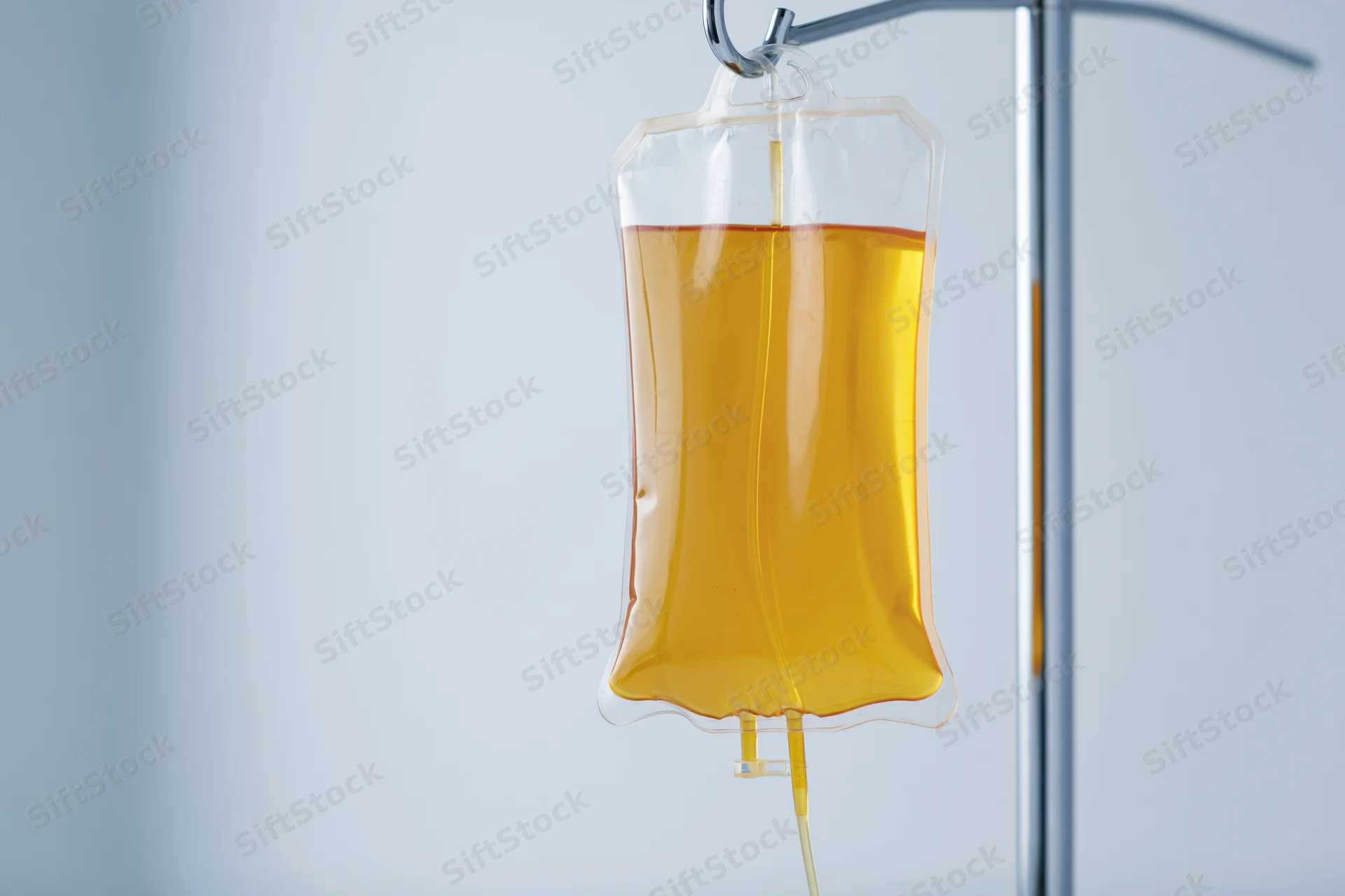 Amber-yellow iv fluid bag hanging from chrome medical stand