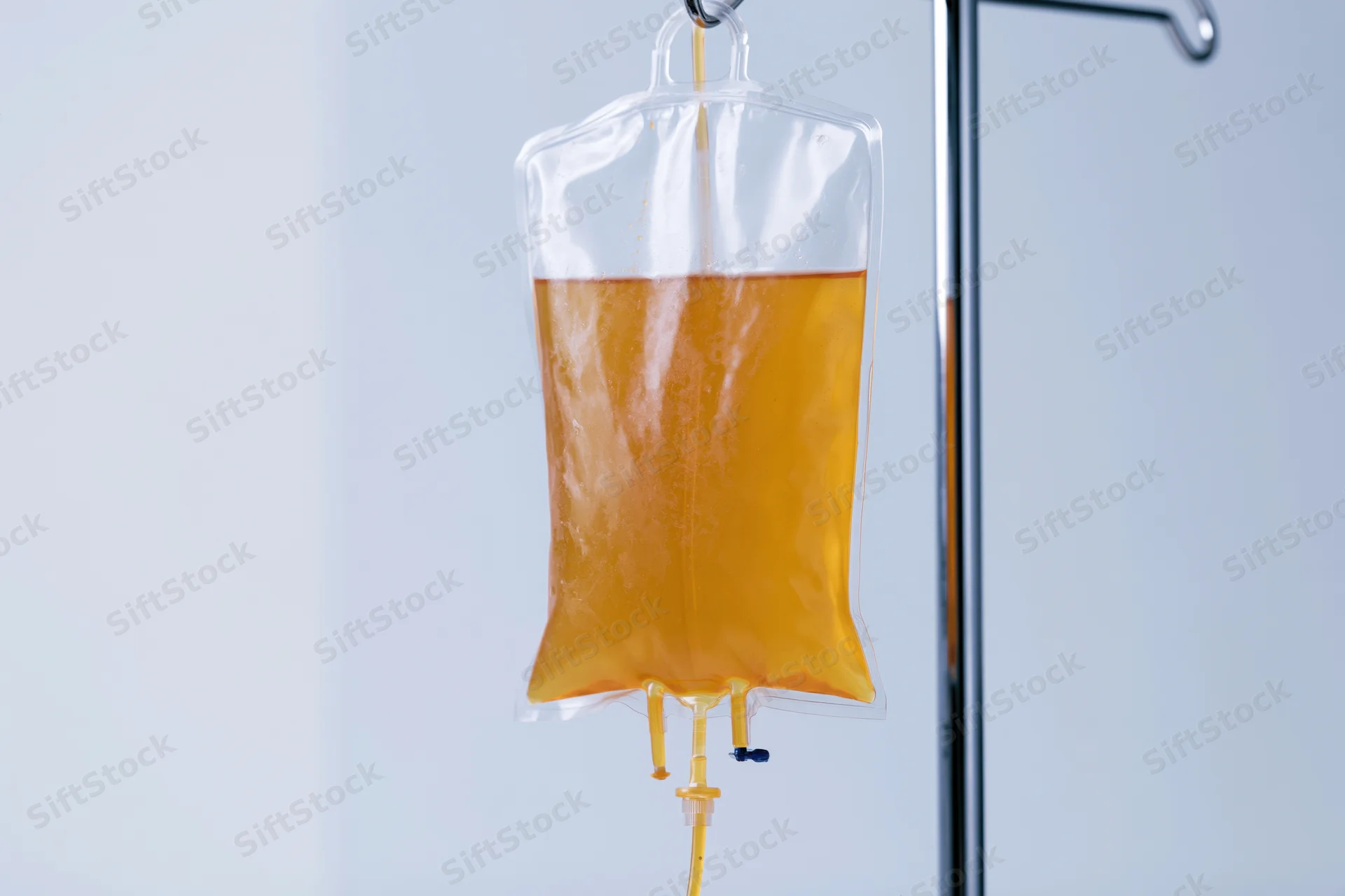 Amber-yellow iv fluid bag hanging from chrome medical stand