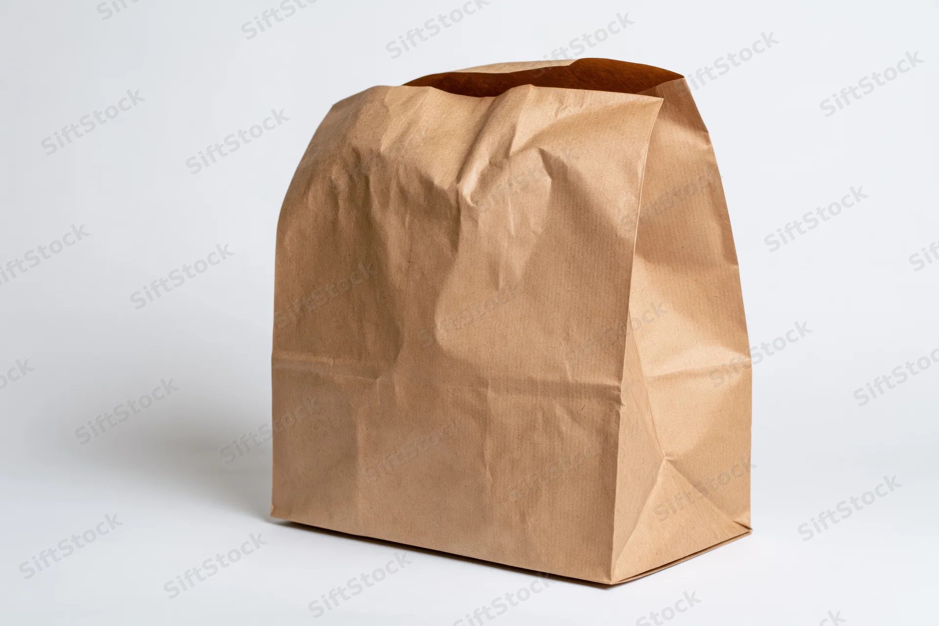 Open brown kraft paper bag standing upright with crumpled texture on white background