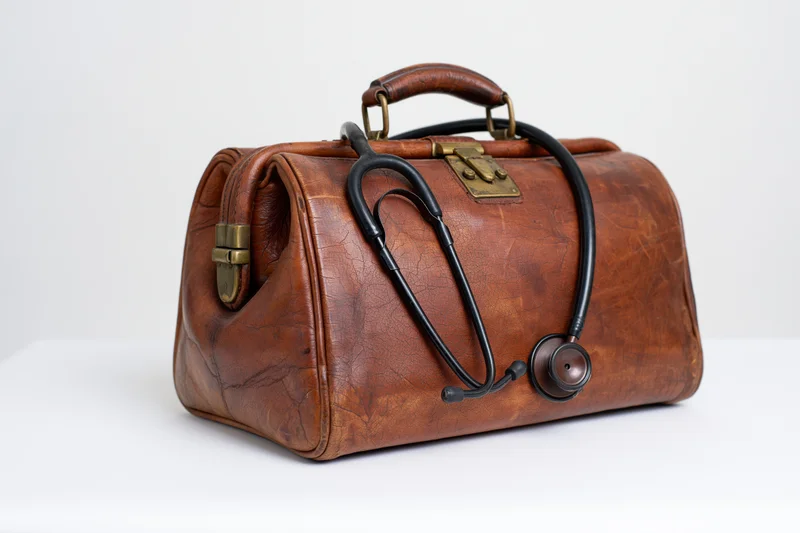 Vintage brown leather doctor's bag with black stethoscope resting on top, isolated on white background