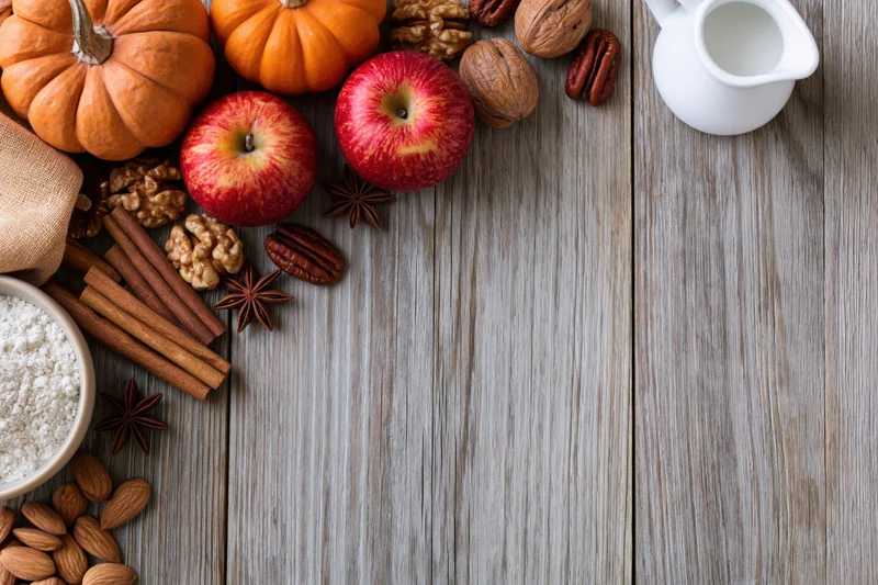 Autumn baking ingredients arranged along left edge of wooden table with copyspace