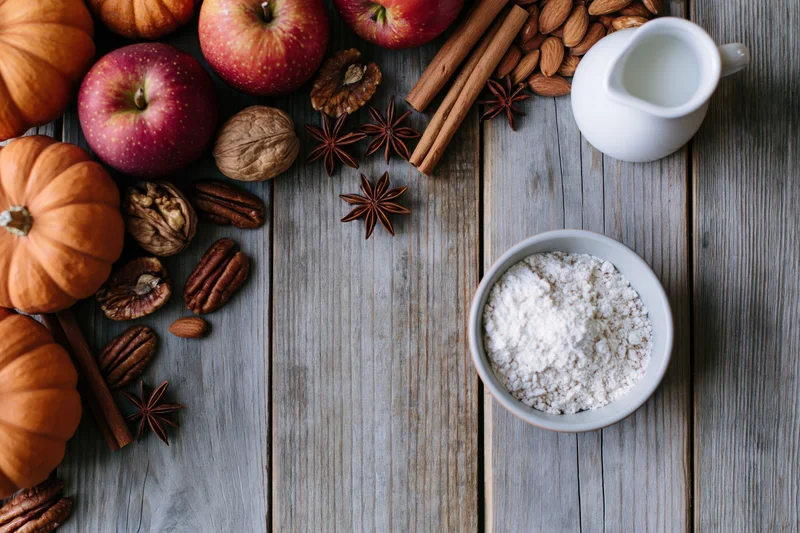 Autumn baking ingredients arranged along left edge of rustic wooden table with copyspace on right