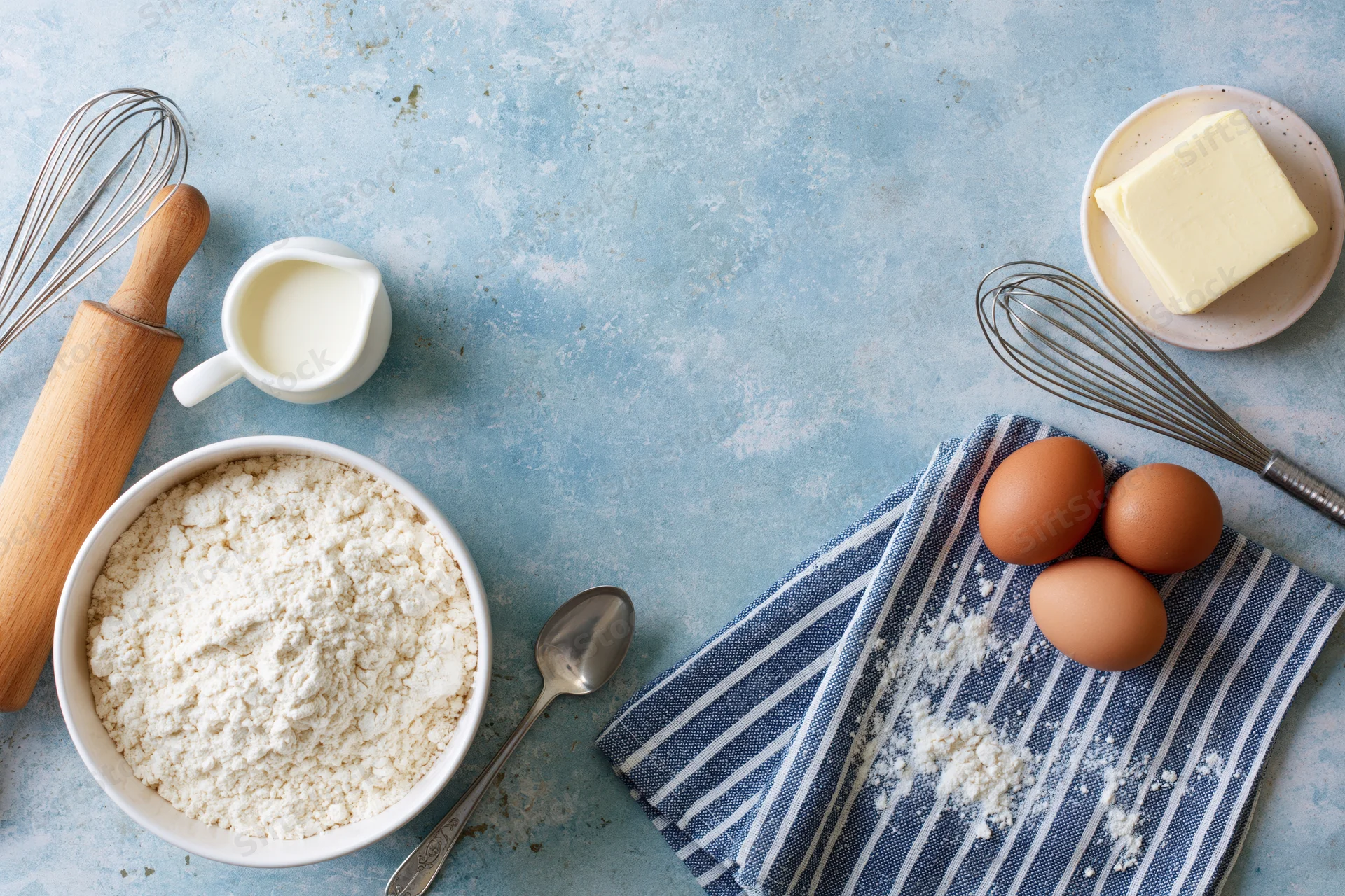 Baking ingredients arranged as a flat lay border on a pale blue surface with copyspace