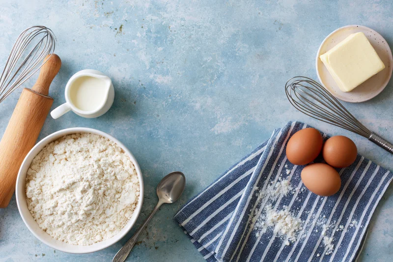Baking ingredients arranged as a flat lay border on a pale blue surface with copyspace