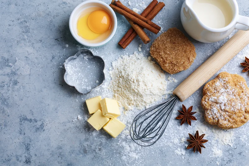 Baking ingredients arranged on a flour-dusted countertop with cookie cutter, whisk and rolling pin