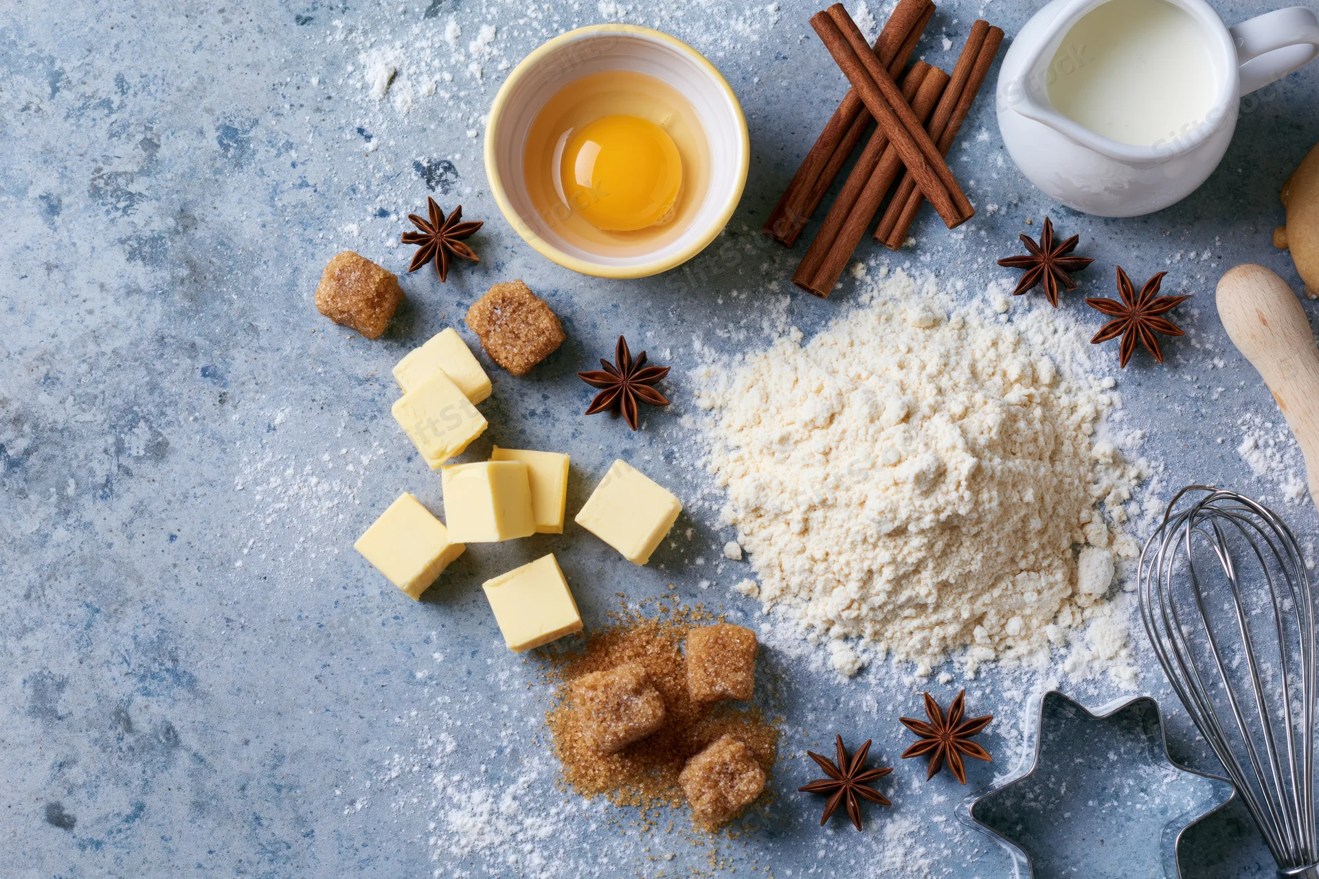 Baking ingredients arranged on a flour-dusted countertop with egg, butter, sugar, cinnamon and milk