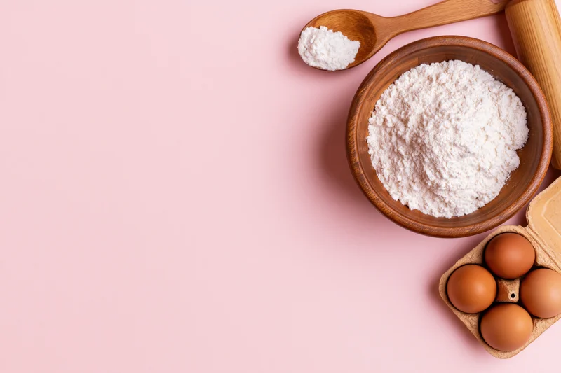 Baking ingredients arranged in upper right corner on pink surface