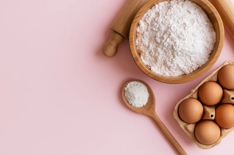 Baking ingredients arranged in upper right corner on pink surface with copyspace