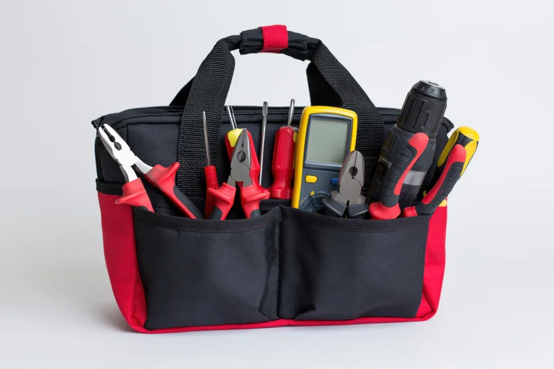 Black and red nylon tool bag filled with electrician's hand tools on white background