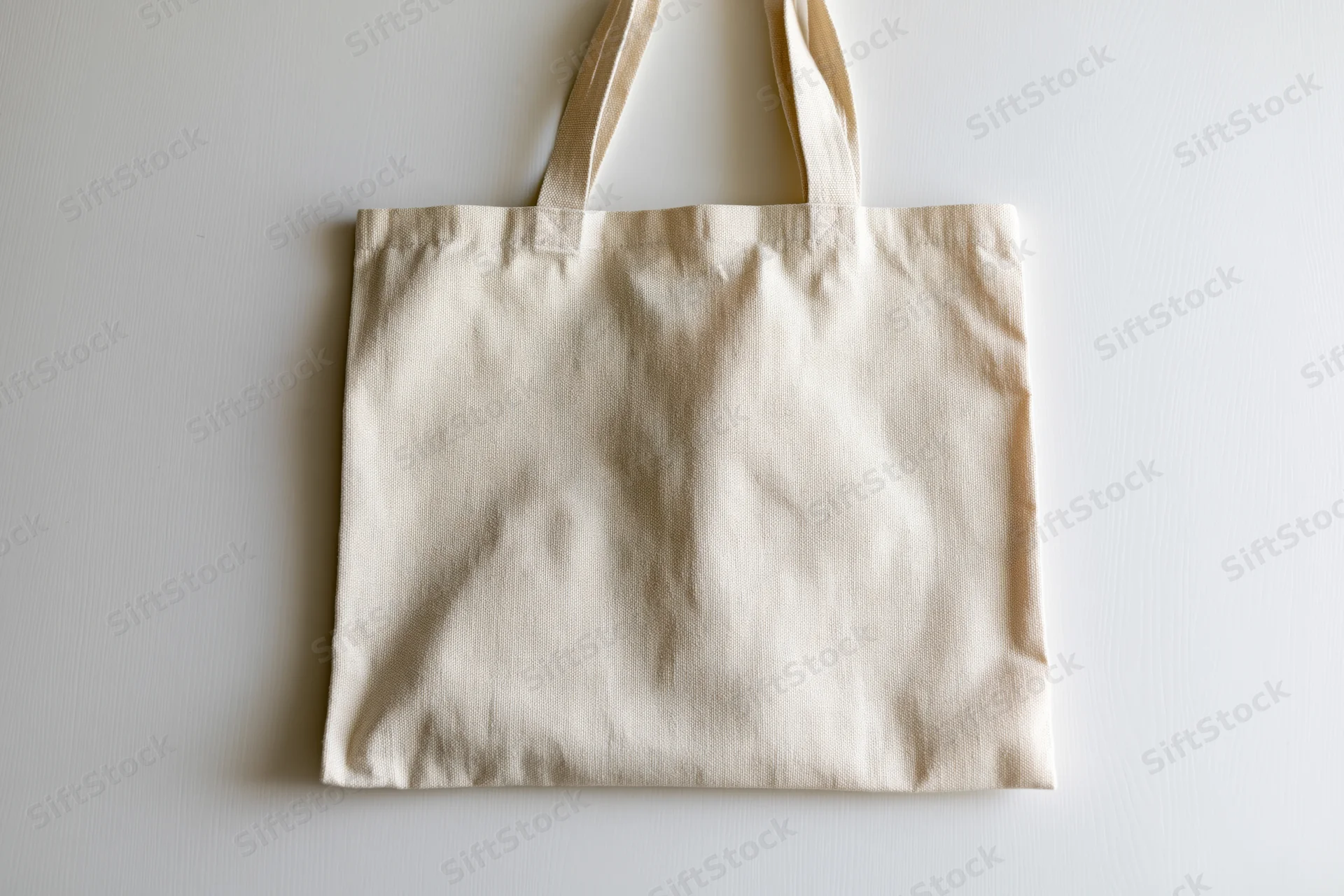 Cream canvas tote bag laid flat on off-white surface with copyspace