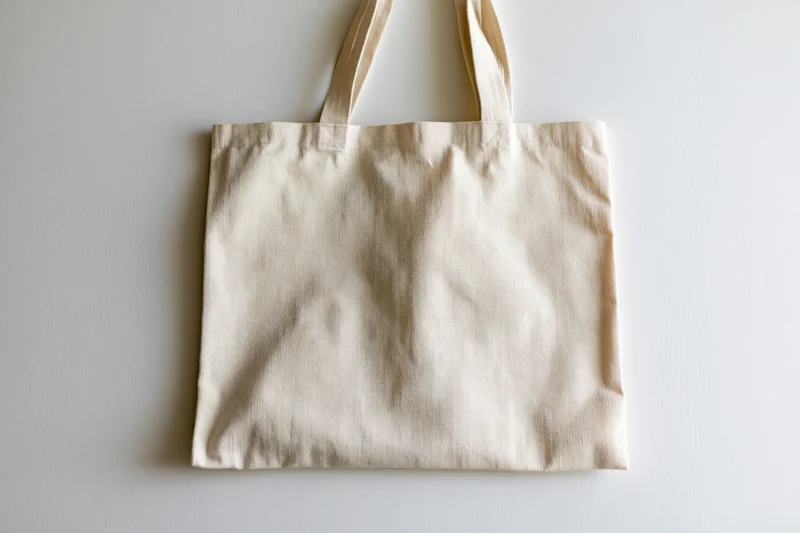 Cream canvas tote bag laid flat on off-white surface with copyspace