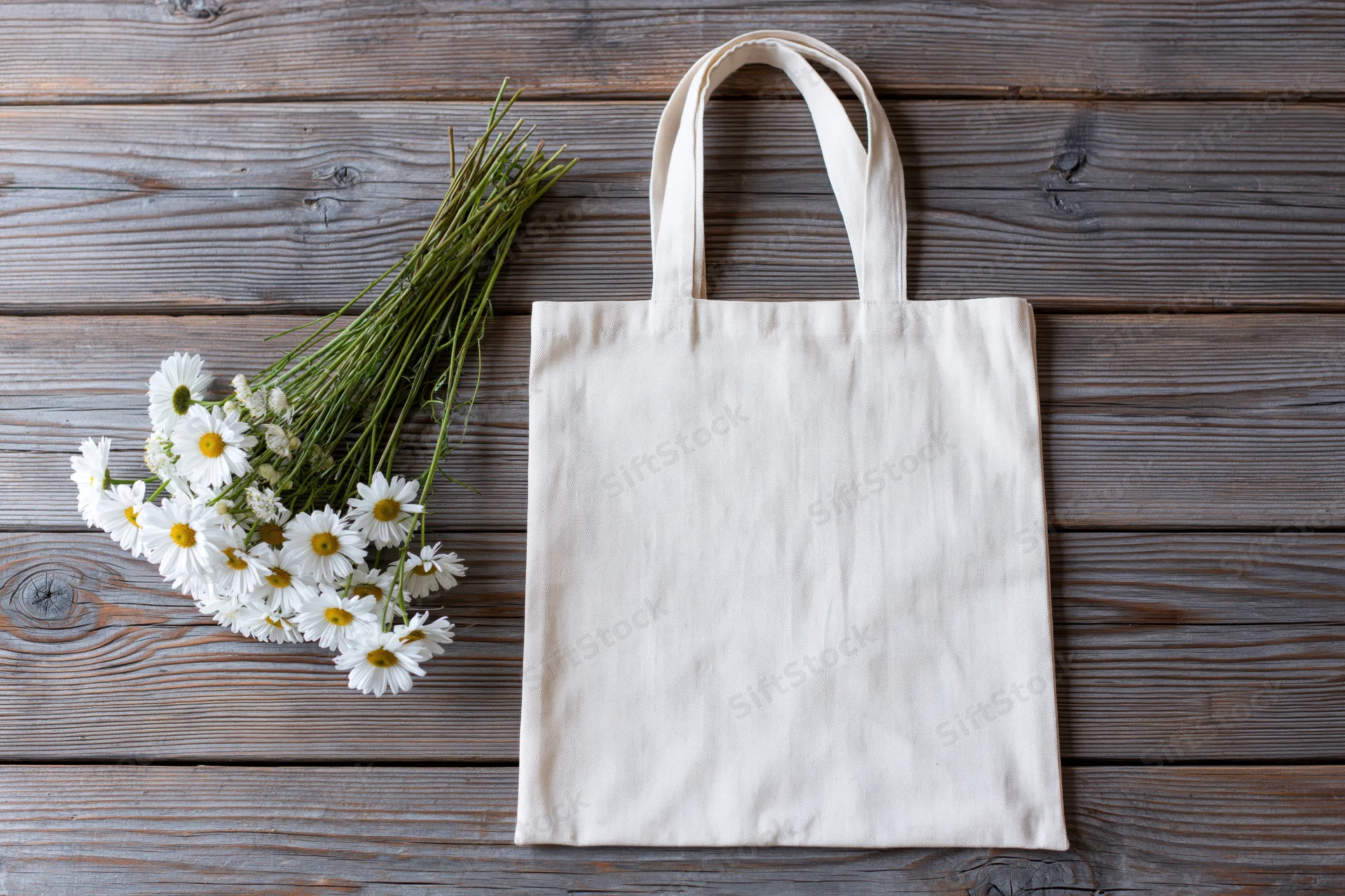 Cream canvas tote bag lying flat next to a loose bunch of daisies on wooden surface