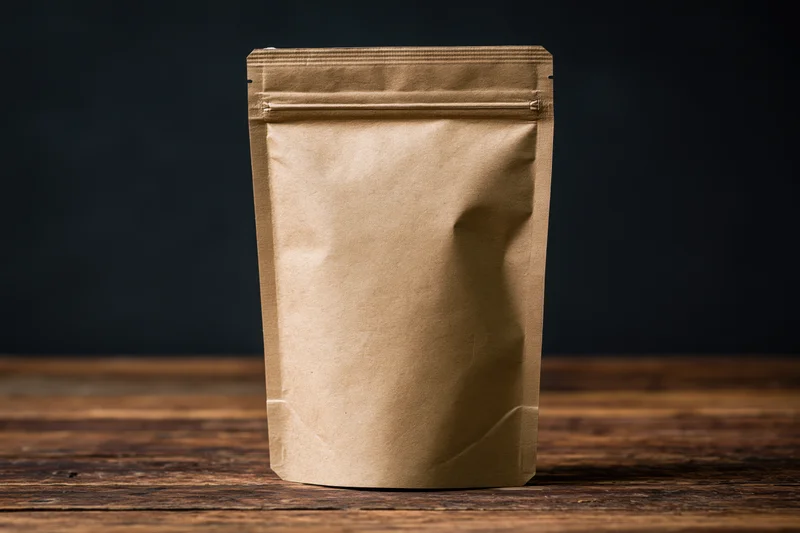 Brown kraft paper pouch standing upright on wooden table against dark background