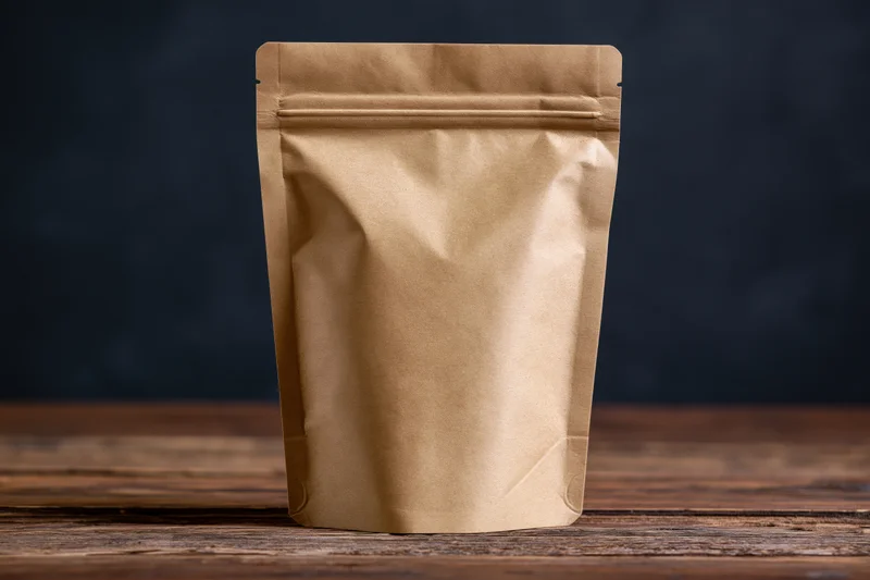Blank kraft paper pouch standing upright on wooden table against dark background