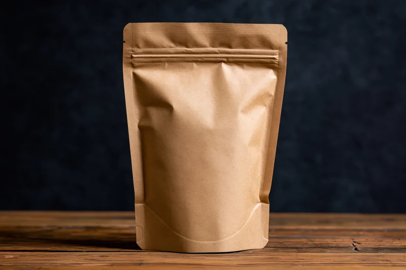 Brown kraft paper standup pouch with zip closure standing upright on wooden surface against dark background