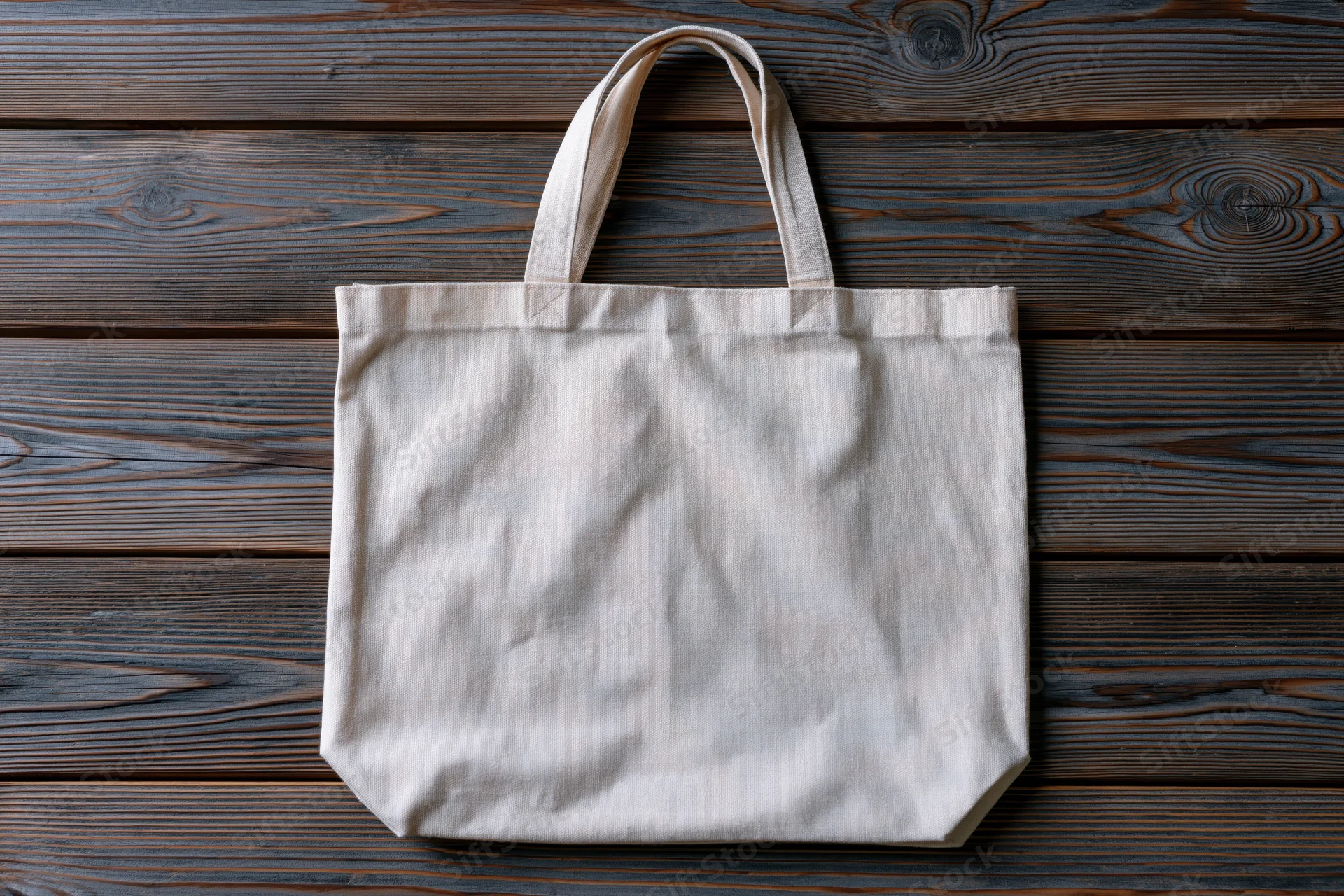 Blank natural canvas tote bag lying flat on weathered wooden surface
