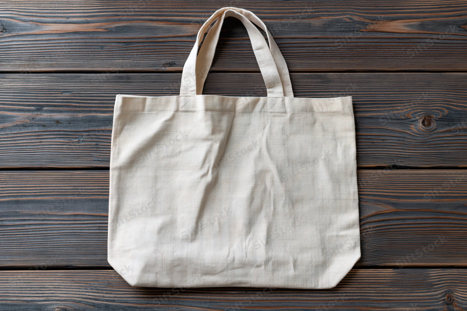 Blank natural canvas tote bag lying flat on weathered wooden surface
