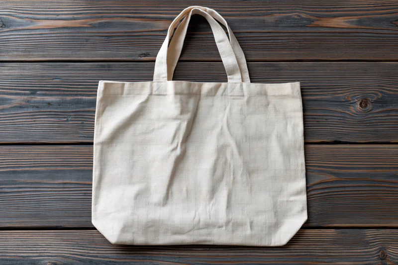 Blank natural canvas tote bag lying flat on weathered wooden surface