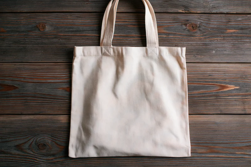 Blank natural canvas tote bag lying flat on weathered wooden surface