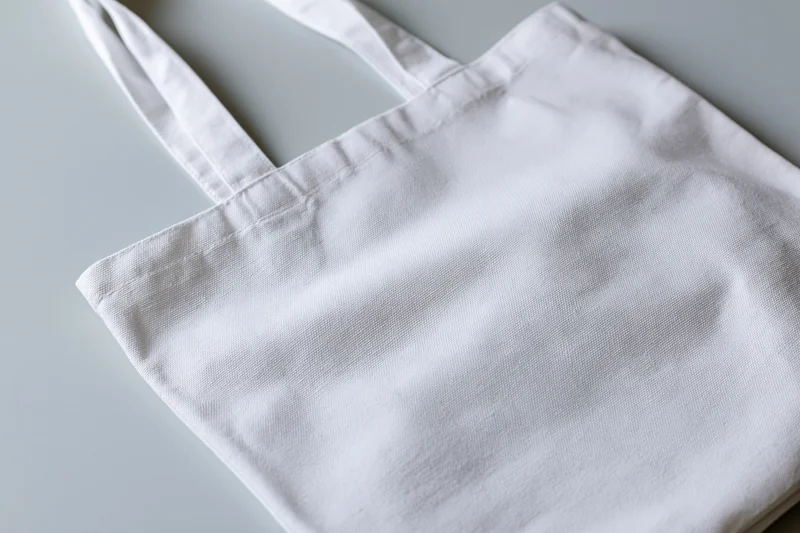 Blank white canvas tote bag lying flat at slight angle on gray surface