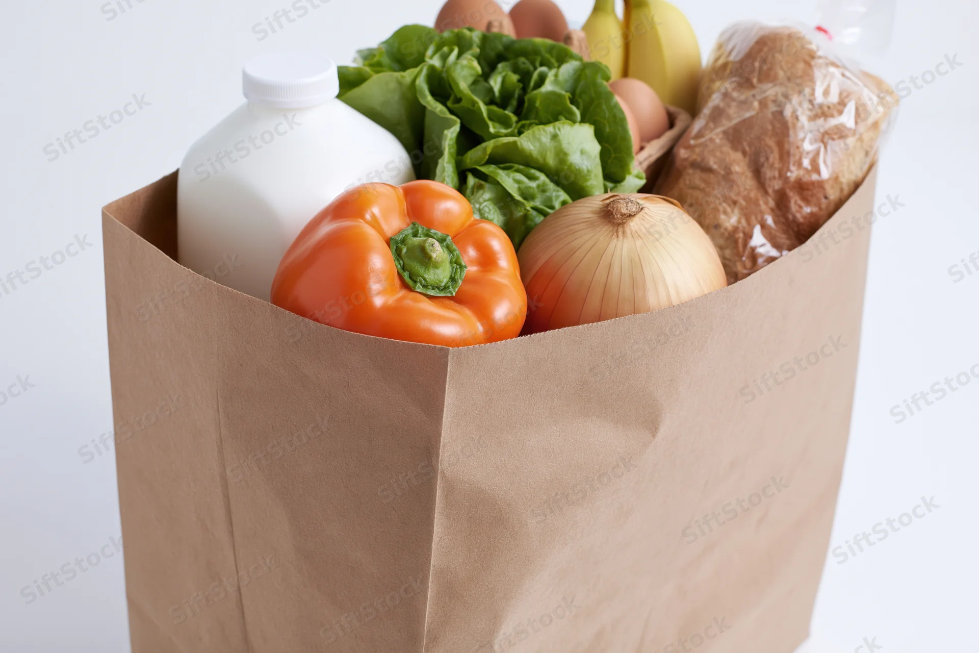 Brown paper grocery bag filled with fresh produce and dairy products on white background