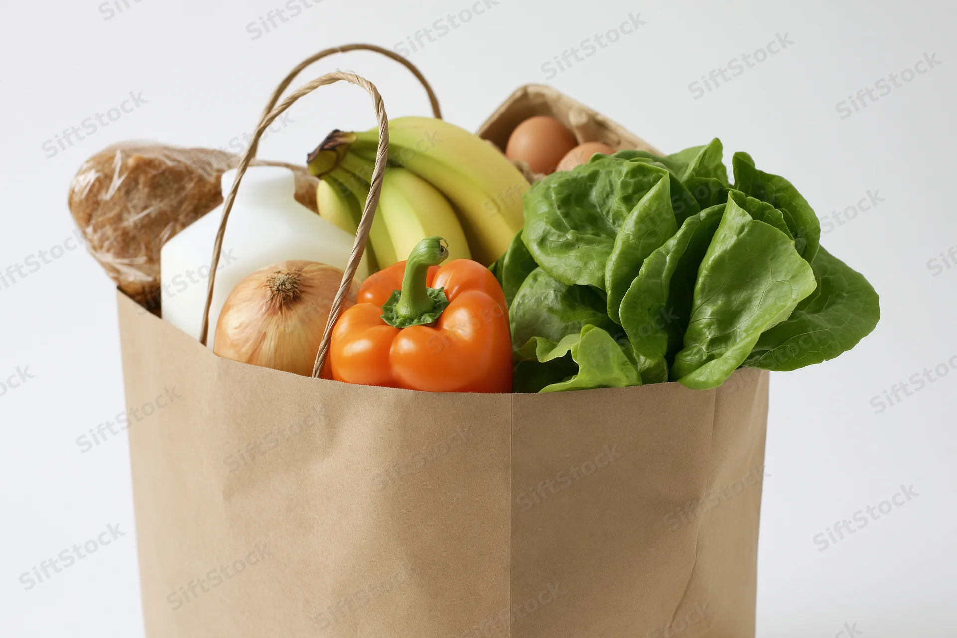 Brown paper bag filled with groceries including vegetables, fruits, milk, bread and eggs against white background