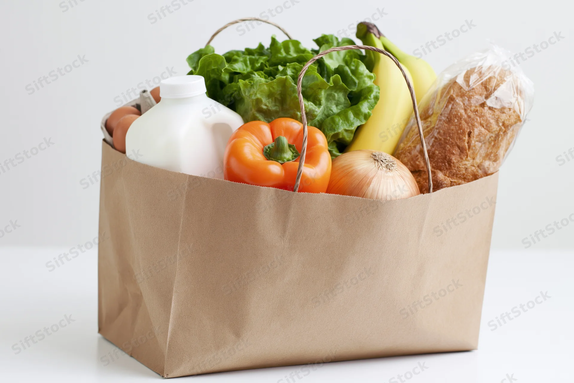 Brown paper grocery bag filled with fresh produce, dairy, bread and eggs on white surface
