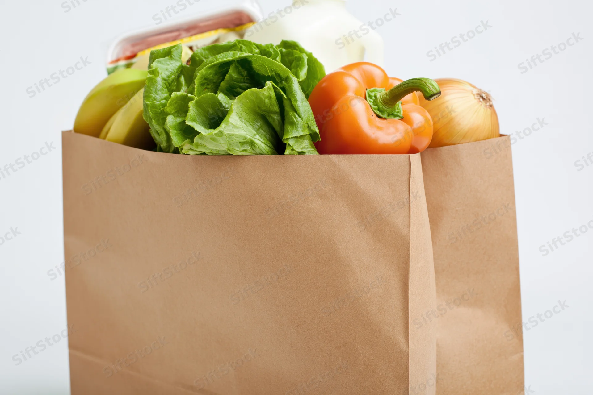 Brown paper grocery bag filled with fresh produce and dairy products against white background