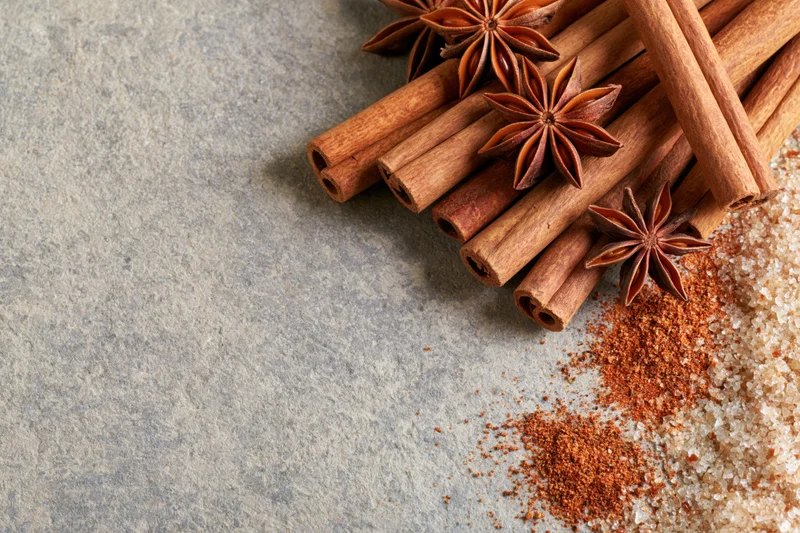 Cinnamon sticks and star anise arranged on a stone surface with ground spice and sugar nearby