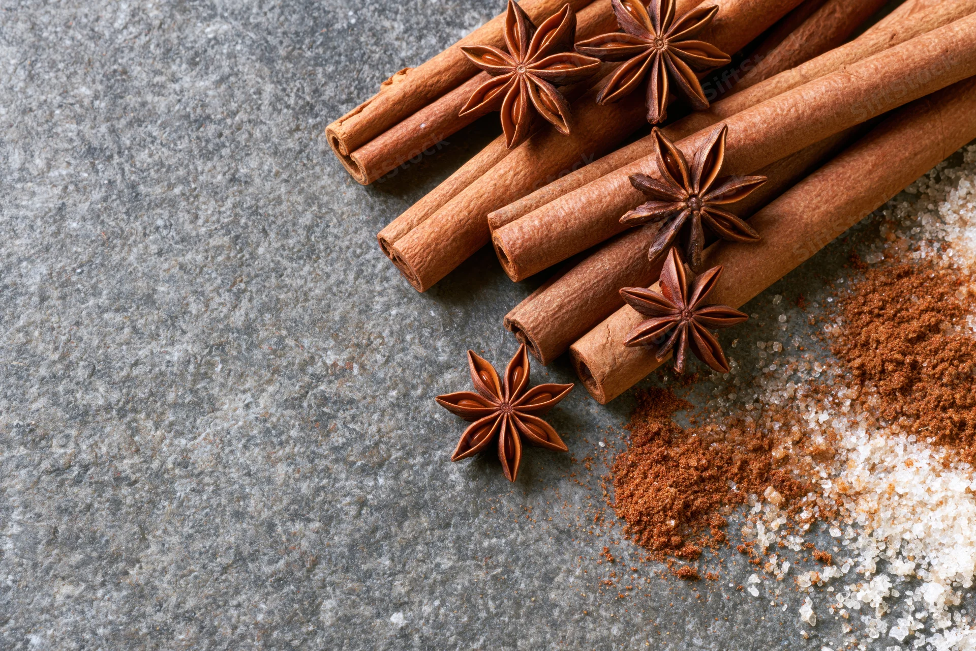 Cinnamon sticks and star anise arranged with ground spice and salt on a gray stone surface