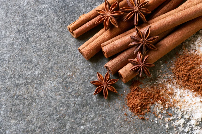 Cinnamon sticks and star anise arranged with ground spice and salt on a gray stone surface