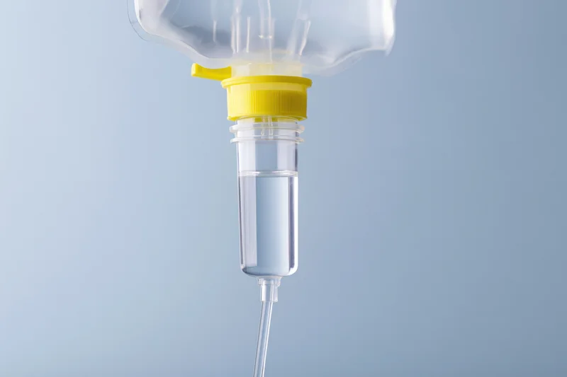 Clear iv saline bag with drip chamber and tubing against blue background