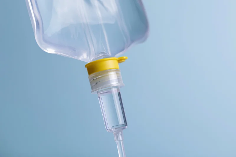 Clear iv saline bag with drip chamber and tubing hanging against blue background