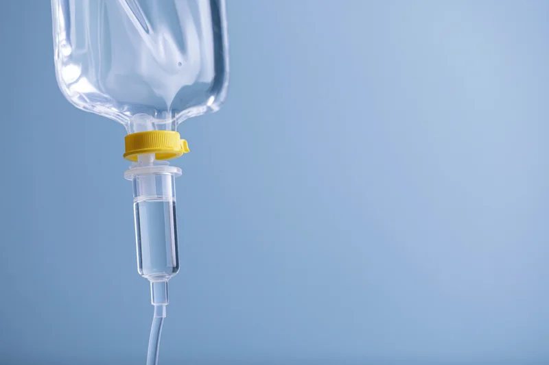 Clear iv saline bag with drip chamber and tubing against blue background