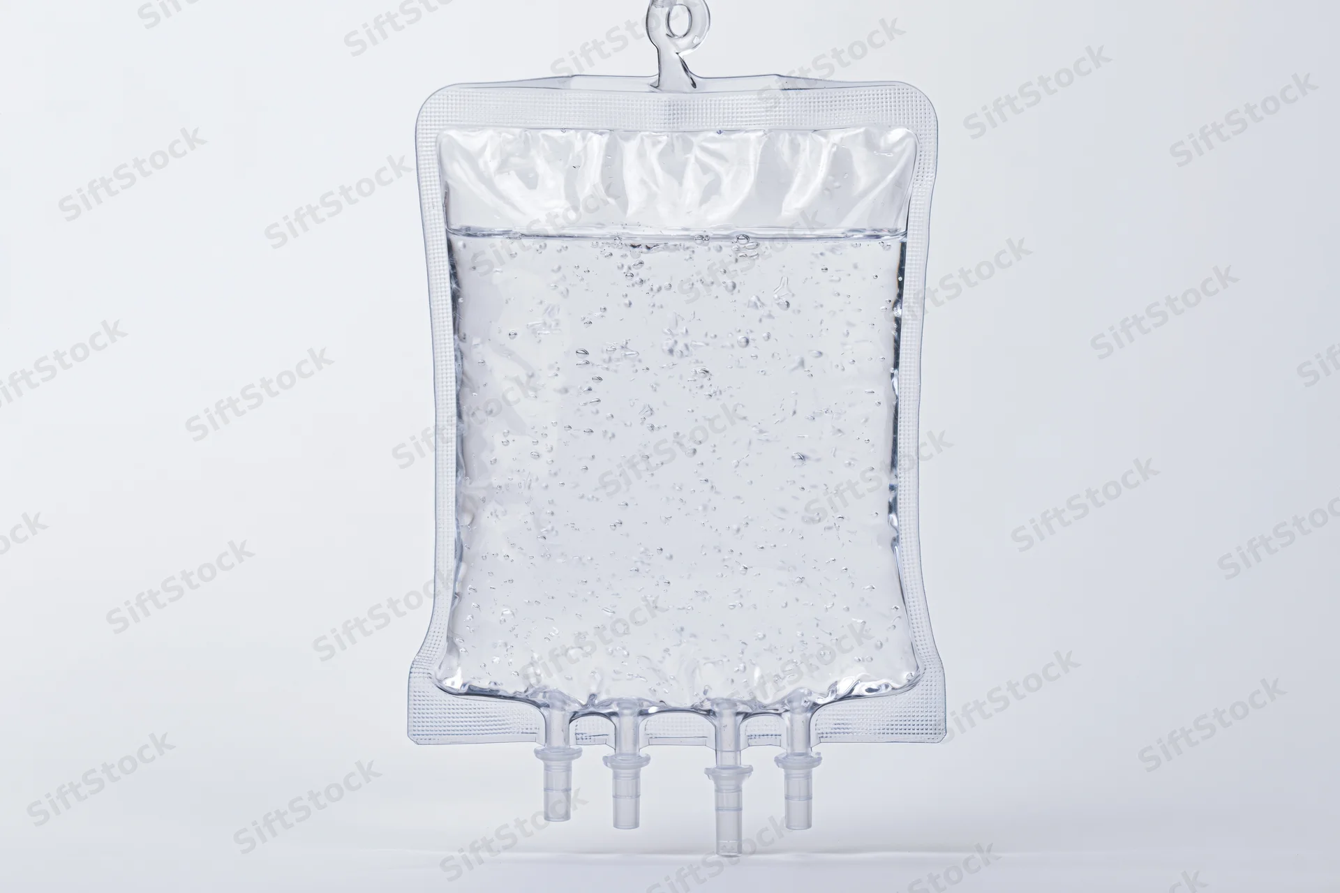 Clear medical iv saline bag filled with transparent fluid hanging against white background