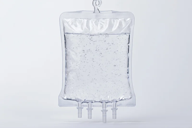 Clear medical iv saline bag filled with transparent fluid hanging against white background