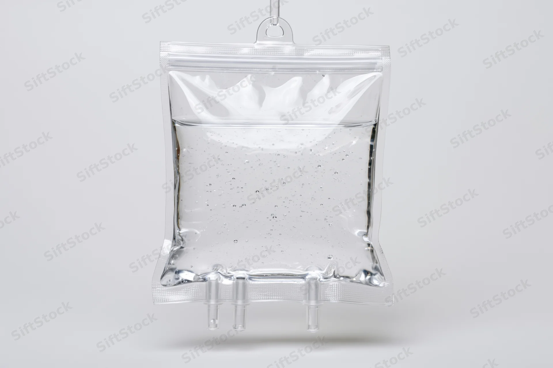 Clear medical iv saline bag filled with transparent fluid hanging against white background