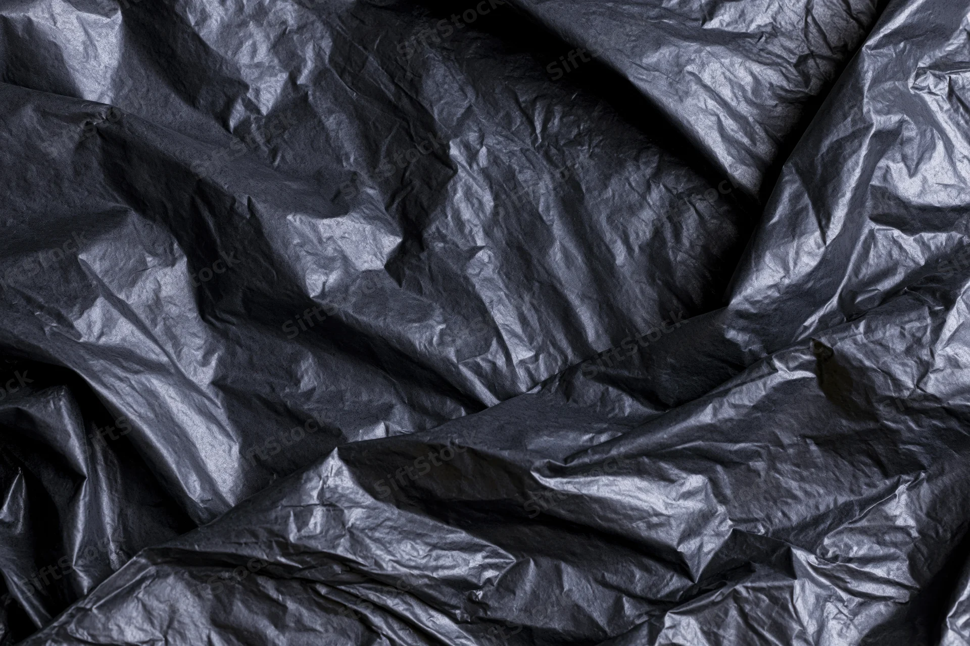 Close-up of heavily crumpled black plastic sheeting laid flat