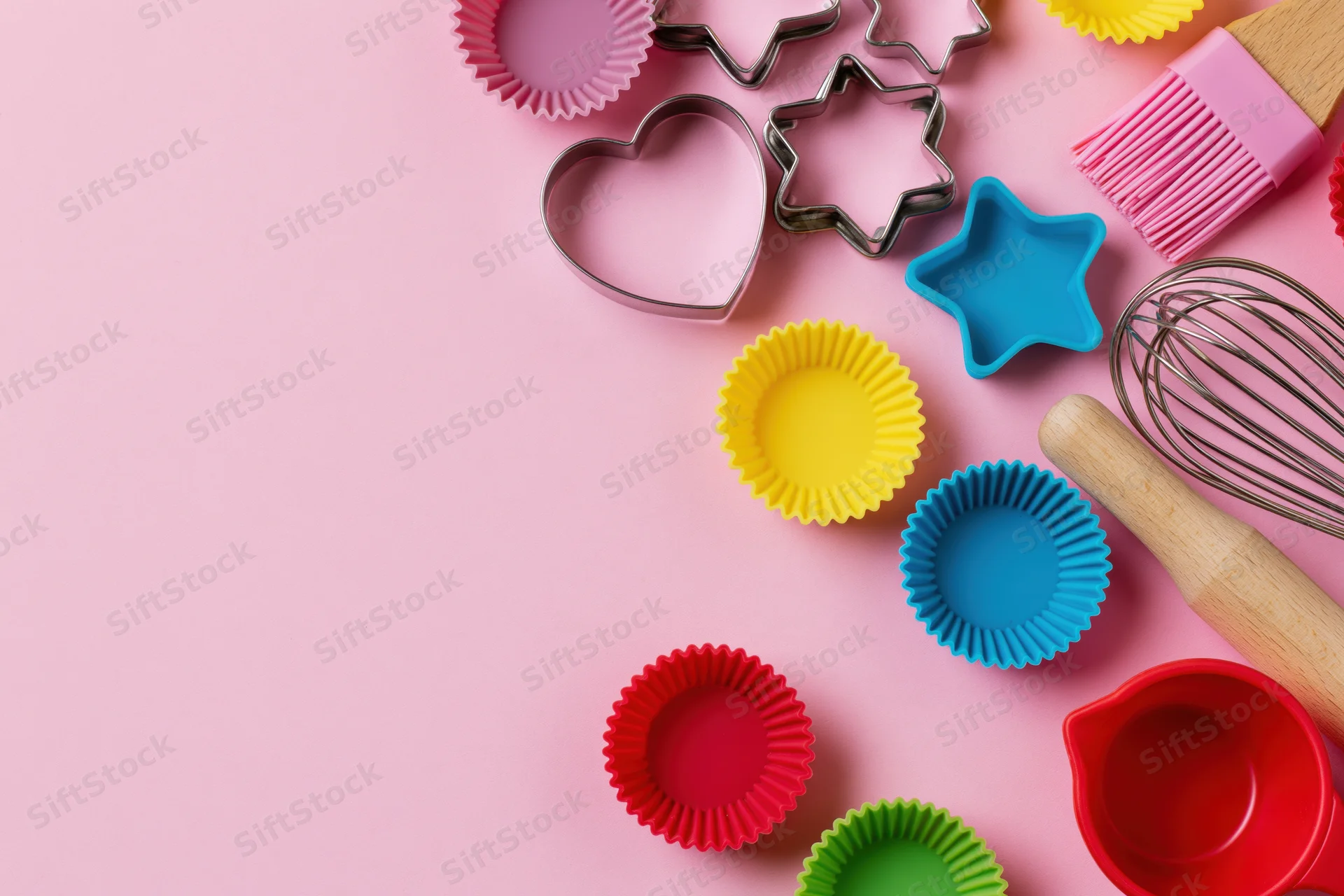 Colorful baking tools arranged in flat lay on pink background with copyspace