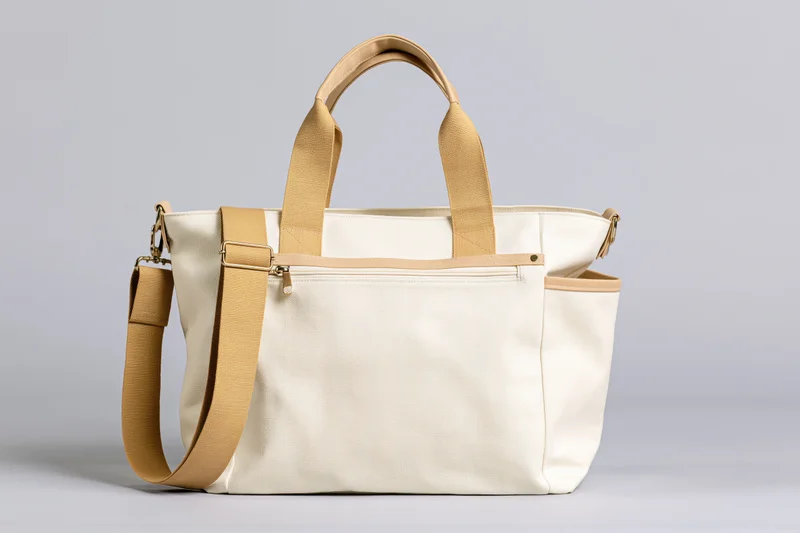Cream canvas tote bag with front zip pocket and open side pocket on plain background